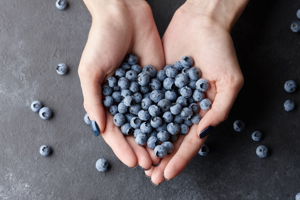 Frau hält Blaubeeren in beiden Händen in Form eines Herzens