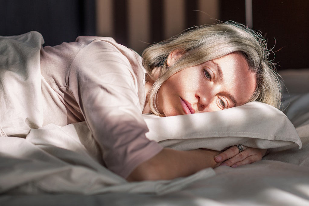 Frau liegt erschöpft und traurig im Bett