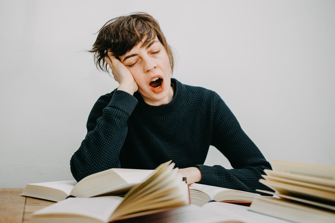 Junge Frau sitzt mit Büchern am Schreibtisch und gähnt 